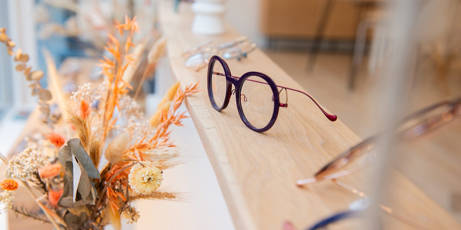 Brille auf hellem Holz neben Trockenblumen